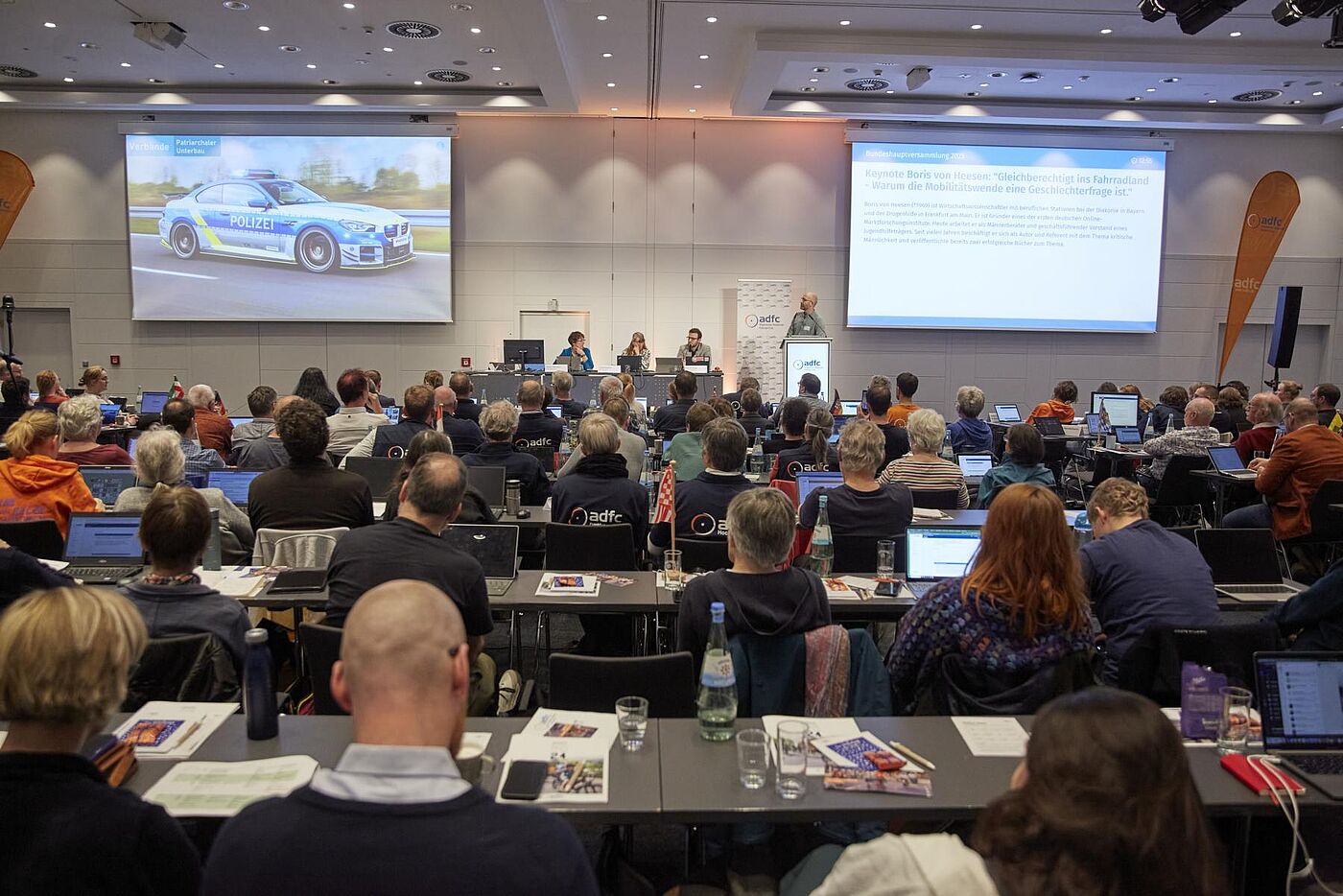 45. ADFC-Bundeshauptversammlung 2025 Teilnehmende sitzen mit Laptops im Saal und hören der Keynote von Boris von Heesen „Gleichberechtigt ins Fahrradland – Warum die Mobilitätswende eine Geschlechterfrage ist“ auf der Bühne mit zwei Projektionsleinwänden zu.